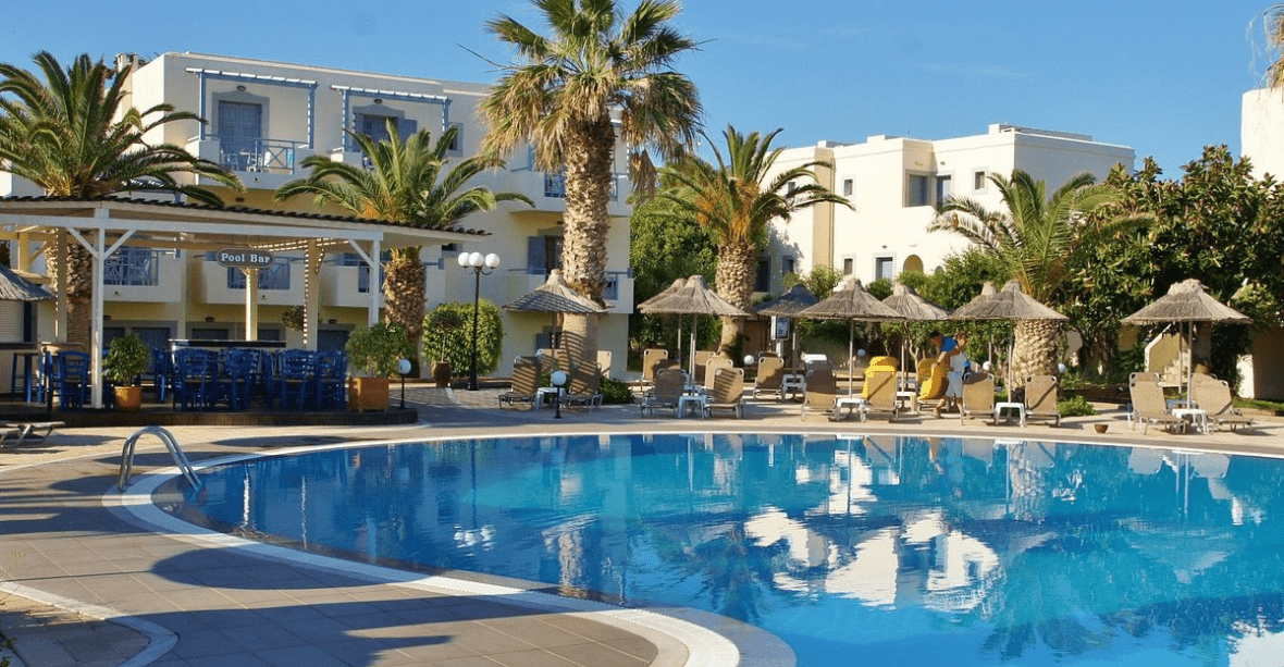 Crète vue de l'Hôtel Europa beach de l'extérieur avec piscine et hôtel en lui-même, palmiers chaises et parasols